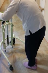 介護施設の廊下で歩行器を使い歩く練習をする女性